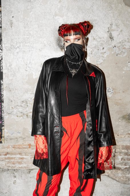 Aurocka como modelo de Morgue Planet con chaqueta de cuero negra con detalles en puntilla y pantalón de chándal rojo con espinas negras