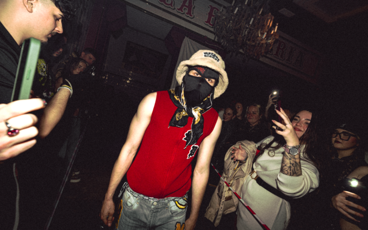 Persona con máscara y sombrero rodeada de gente en un ambiente festivo.