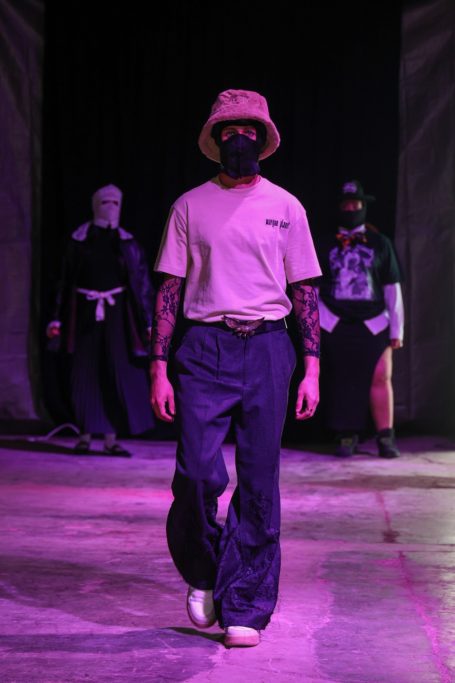 Modelo con camiseta y pantalones anchos, caminando sobre una pasarela con otros tres modelos.