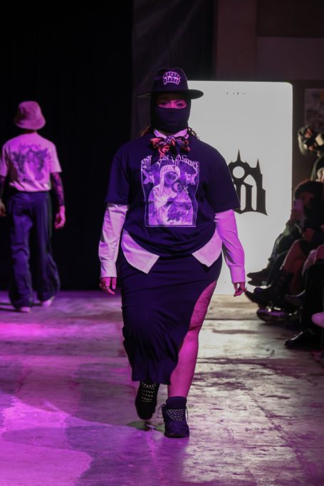 Modelo desfilando en la pasarela con un atuendo negro y complementos llamativos.