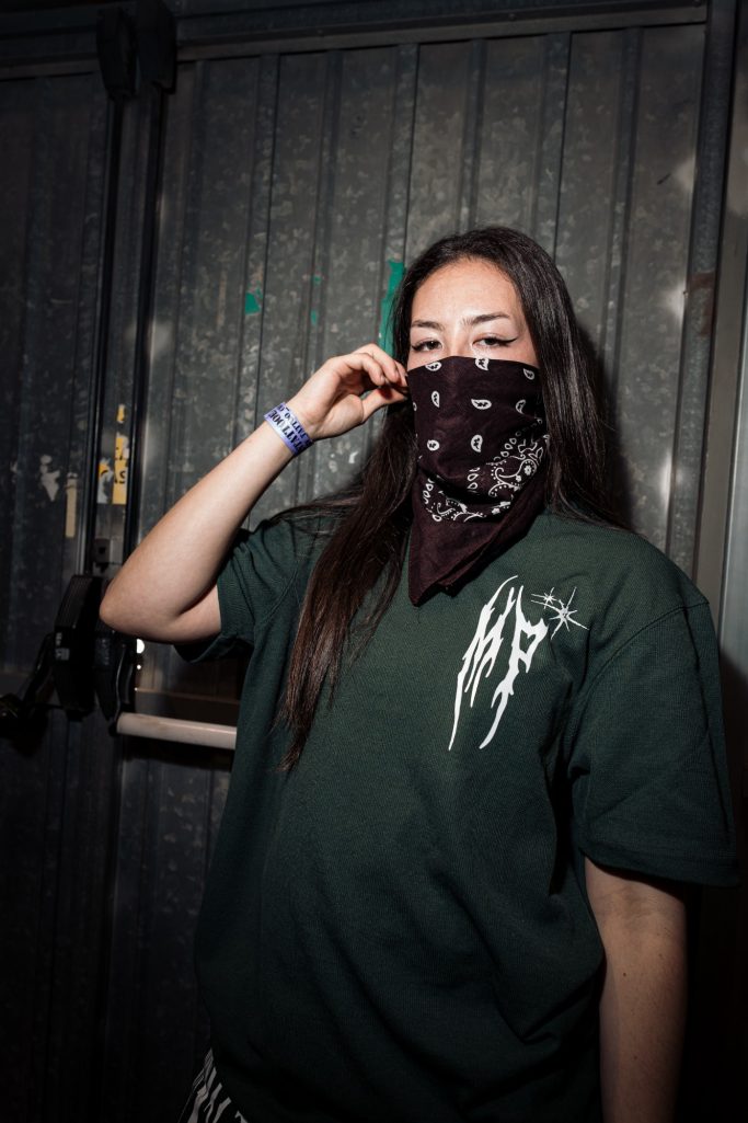 Joven con camiseta verde y pañuelo negro en un ambiente oscuro.