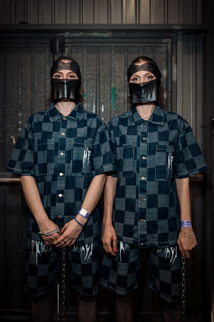 Dos personas vestidas con camisas y pantalones a cuadros oscuros, con máscaras faciales.