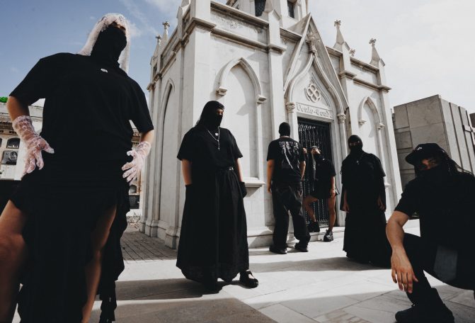 Grupo de personas con ropa oscura y capuchas frente a un edificio religioso.