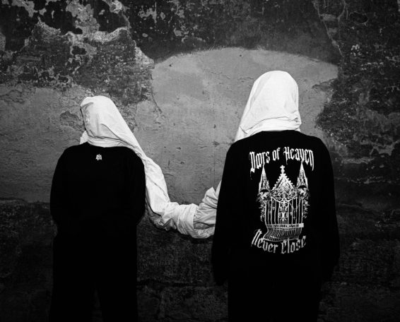 Dos figuras con capuchas blancas y sudaderas oscuras, de espaldas, unidas de la mano.